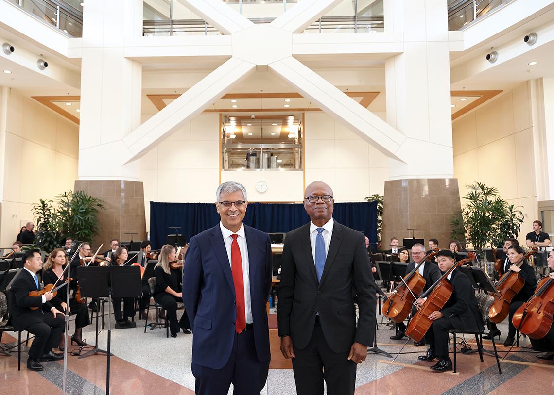 Bhattacharya and Aiyelawo stand in front of full orchestra in the CC atrium.