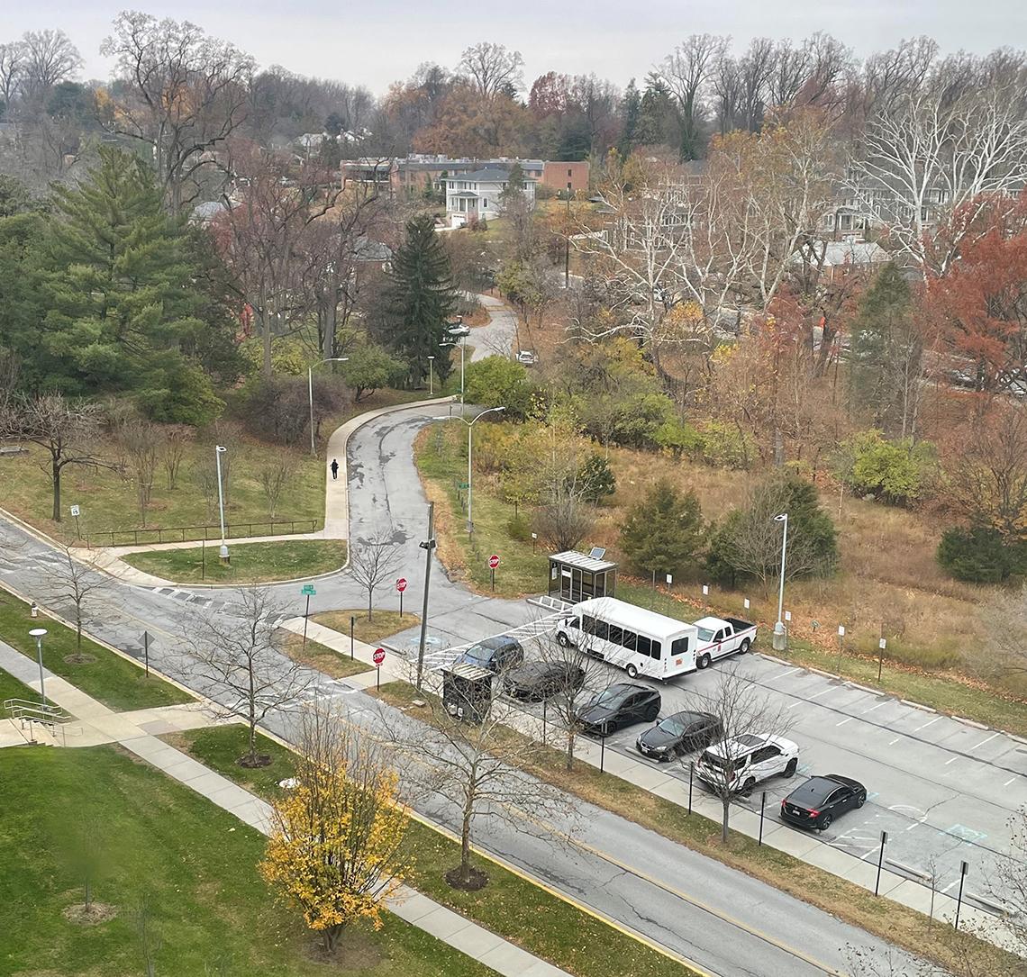 A campus shuttle waits in front of covered shuttle stop in surface lot behind Bldg. 31.