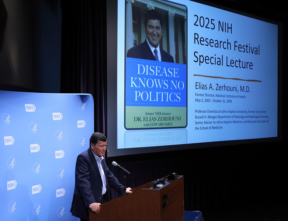 Zerhouni speaks at podium next to large slide on screen with book cover for "Disease Knows No Politics"