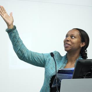 Lash gestures up toward slide as she speaks from behind podium.
