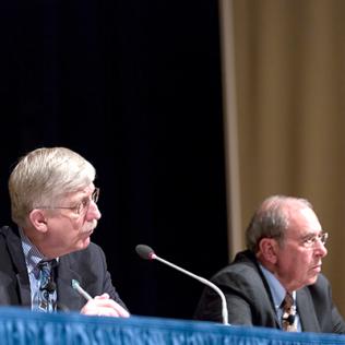 Seated at a panel table on stage, Collins and Gallin listen to people in the audience.