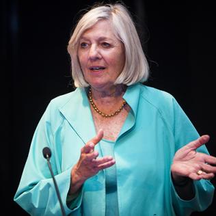 Behind the mic, Goodman gestures with her hands.