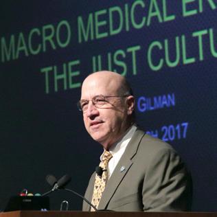 Gilman speaks from podium with slide projected behind him.