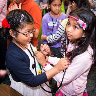 Two young girls listen to each other's heartbeat with stethoscopes