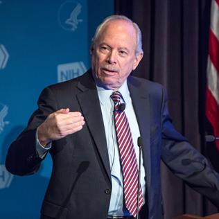 Leshner stands with hand cupped as he speaks at podium. 