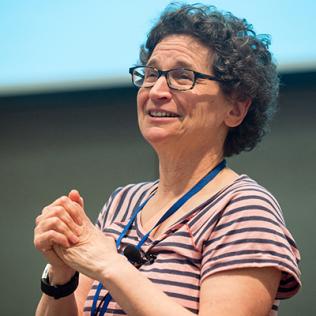 A smiling Dr. Milgram stands on stage with her hands clasped.