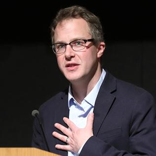 Dr. Christopher Phillips with open hand across his chest speaks at podium.