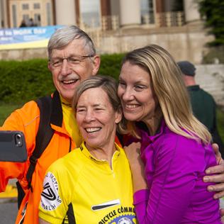 Dr. Collins hold out cell phone to take photo with his family in front of bldg. 1