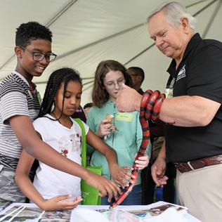 Kids pet a red and black snake that's wrapped around its owner's arm.