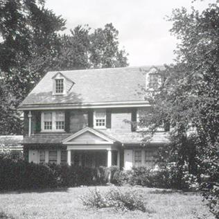 A 2-story house with yard, shrubs and trees