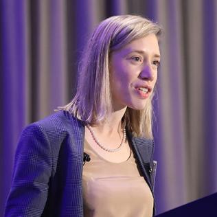 Baker stands at podium in Bethesda Hyatt ballroom.