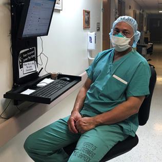 Dr. Chinquee in a mask and scrubs sits by a computer in a Clinical Center hallway.
