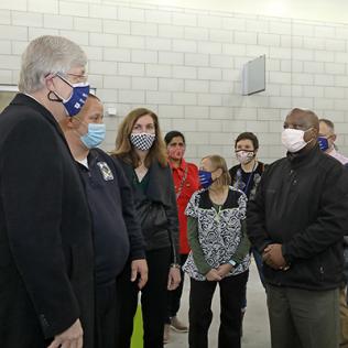 Collins greets several other employees standing in a semi-circle, with masks on.