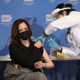 Seated with left arm exposed, Harris receives a shot in the arm from Chan.