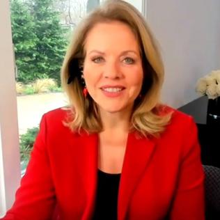 A smiling Renee Fleming wearing a red blazer speaks from her home.