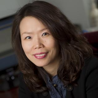 A smiling Mi-Kyung Song sits with arms resting on table