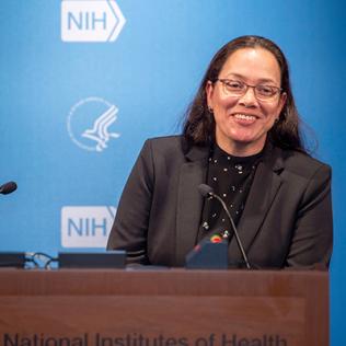 A smiling Quiroz stands at podium in Lipsett Amphitheater