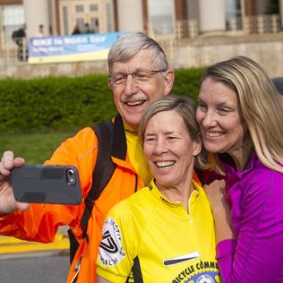 In front of Bldg. 1, Collins, in bike-riding gear, takes a selfie with wife Diane Baker and daughter Margaret