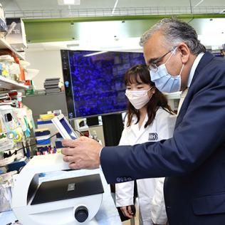 Jha leads over equipment as Woo in labcoat looks on.