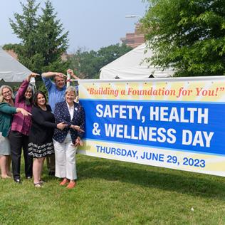 NIH leaders hold up Safety, Health & Wellness Day 2023 poster outside on the lawn