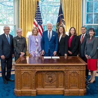 President Joe Biden and First Lady Dr. Jill pose with women's health advocates behind desk in Oval Office.