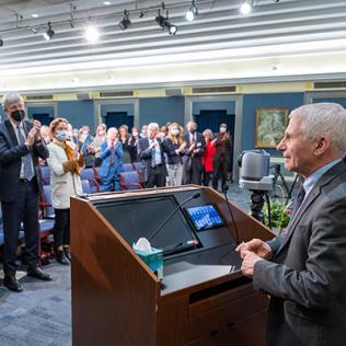 Fauci at podium faces standing attendees 