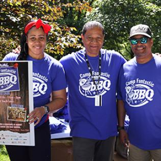 Three Camp Fantastic supporters pose with a poster advertising the BBQ.