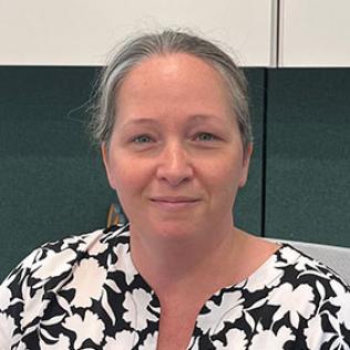 A smiling Keegan, wearing a patterned black-and-white shirt, seated in an office.
