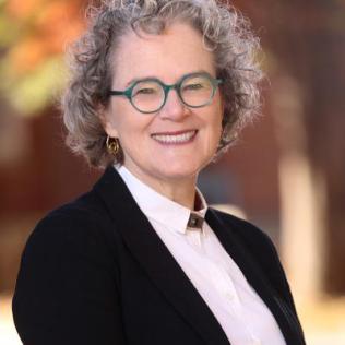 Marrazzo smiles at the camera. She has short, curly gray hair and teal glasses.