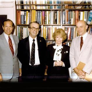 Three men and one woman stand in front of a bookcase.