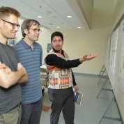 Calac points to poster, talks to two colleagues.