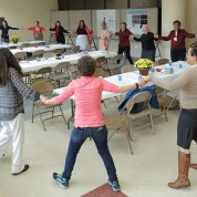 Colleagues hold hands, stand in circle in large room, ready to dance.