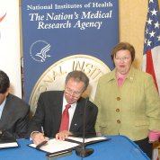 Mikulski stands alongside Katz as NIH and NASA leaders sign agreement at table.
