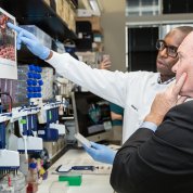 Mulangu gestures toward poster as Coons looks on.
