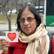 With Metro station in background, woman holds up red heart sticker.