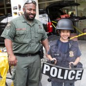 An officer poses with kid dressed in helmet and police shield on the Bldg. 31 patio.