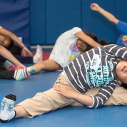 Kids, with legs wide, reach for their toes in an NIH fitness class.
