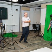 Woman with virtual reality goggles gestures in front of green screen as man observes