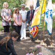 Woman places flower at stone marker as several people look on