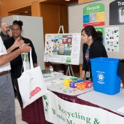 Man receives reusable tote bag from woman behind an information table