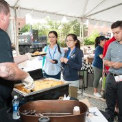 Under a tent, a food vendor serves several patrons.
