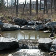 A waterfall flows from a small creek, surrounded by boulders, trees on the NIH campus