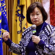 With U.S. and department flags in the background, Fugh speaks into microphone