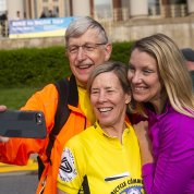Dr. Collins hold out cell phone to take photo with his family in front of bldg. 1