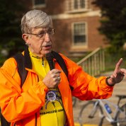 A brightly dressed Dr. Collins holds microphone to address crowd.