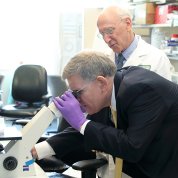 Droegemeier looks through a microscope as Rosenberg stands beside him 