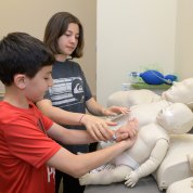 Two children practice CPR chest compressions on an infant mannequin.