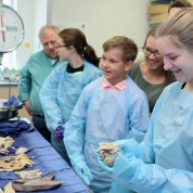 A smiling teenage girl wearing gloves holds a human organ in the autopsy suite.
