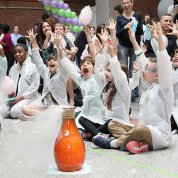 Smiling kids throw hands up and cheer as they watch an orange bottle fizz during a science experiment.