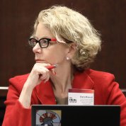 Dr. Bianchi looking off to the side sits in front of laptop holding a pen